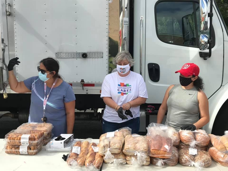 Photo of three Loudoun Cares staff and volunteers giving bread and pastries spread out over a large table.
